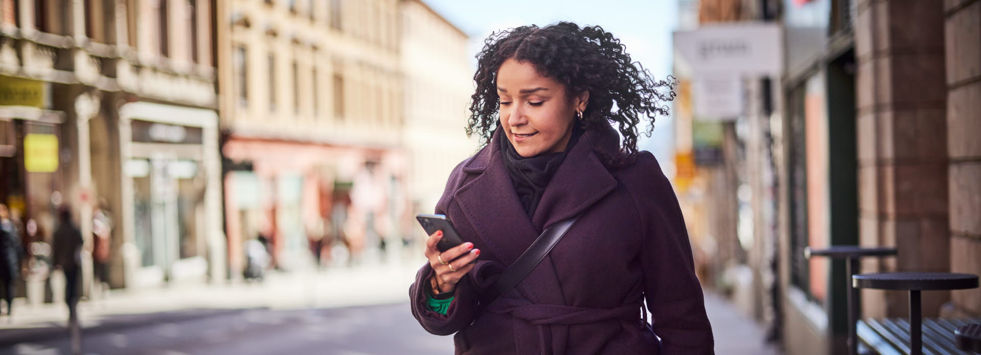 Woman walking in the city with a phone in her hand. ITAB creating seamless online and offline consumer journeys.